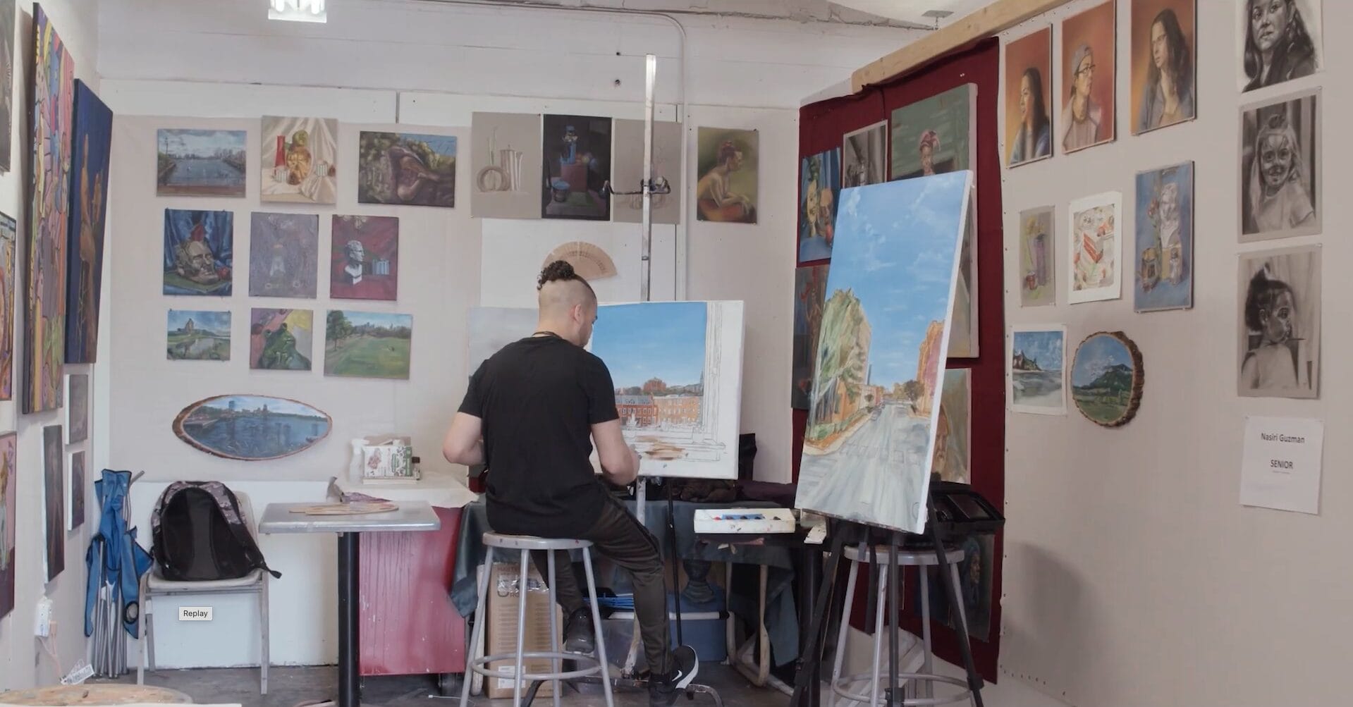 A student sits at a canvas in his painting studio